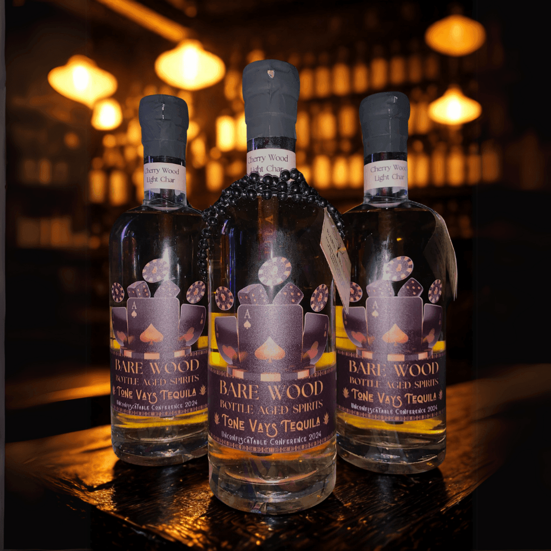 Three bottles of Bare Wood aged tequila on a wooden surface with a dimly lit background.
